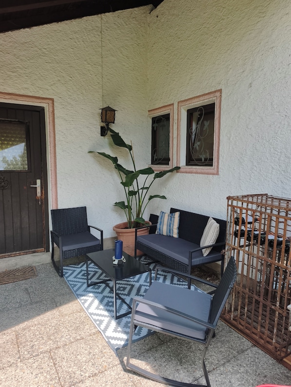 An outdoor seating area with a sofa, two chairs, a table, and a potted plant.