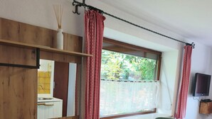 Una habitación con un escritorio de madera, dos sillas, una mesita, un televisor y una ventana con cortinas.
