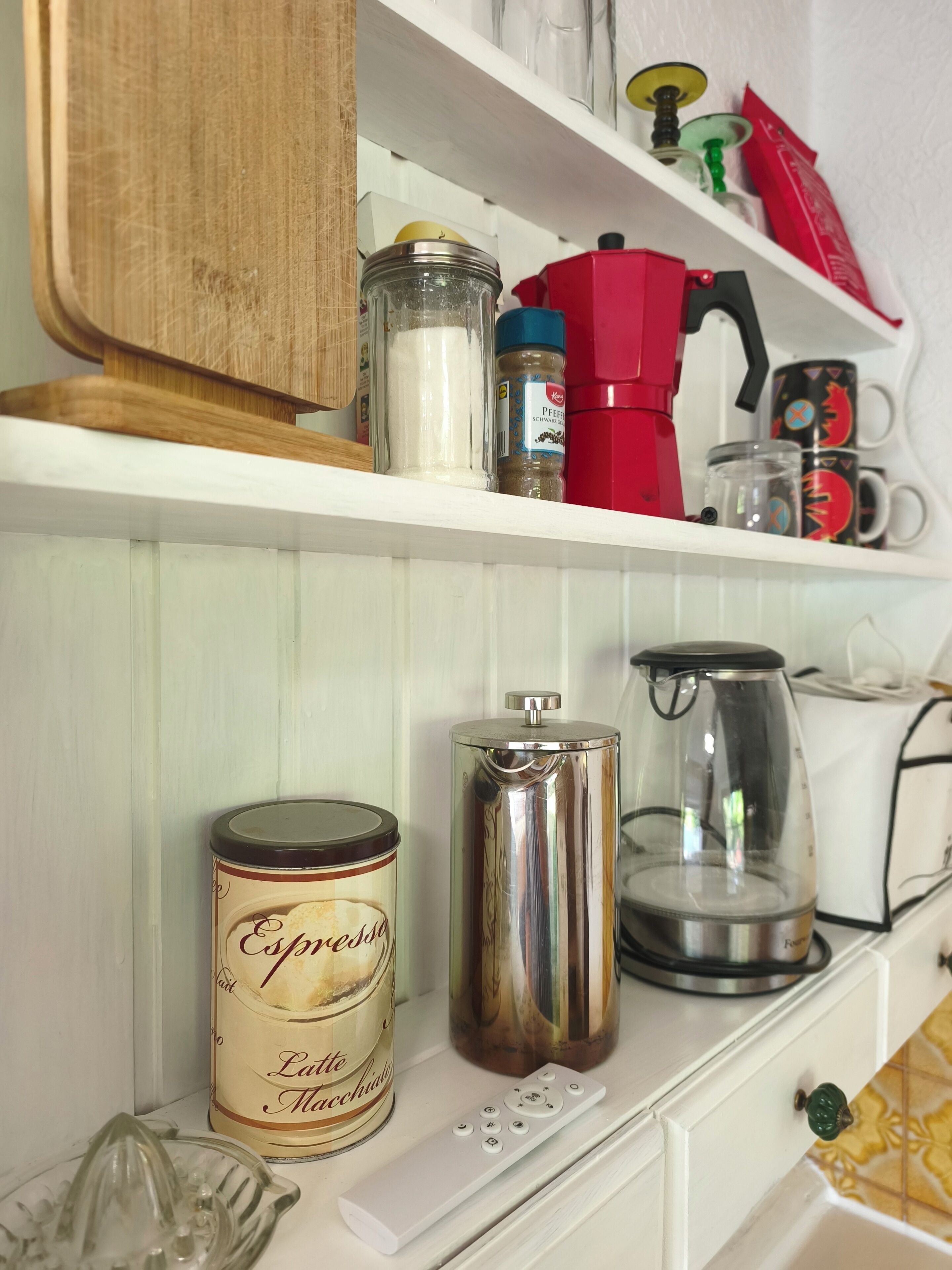 A kitchen shelf with a coffee maker, a jar of sugar, a spice container, and a can of espresso.