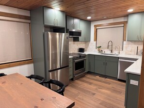 Eine moderne Küche mit Edelstahlgeräten, grünen Schränken und einem Holzessttisch.