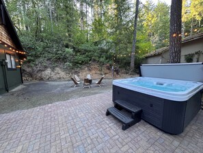 Ein Whirlpool mit Holzterrasse, umgeben von Bäumen und einer Pflasterterrasse.