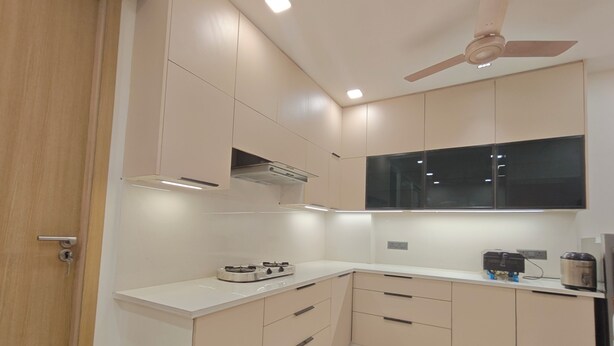 A modern kitchen with beige cabinetry, a gas stove, a ceiling fan, and a window above the countertop. - Peaceful 3 BHK Stay with Premium Amenities (Lucknow)