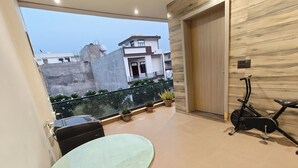 A balcony with a glass table, potted plants, and a stationary exercise bike. - Peaceful 3 BHK Stay with Premium Amenities (Lucknow)