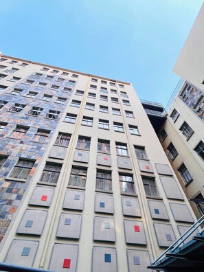 Ein mehrstöckiges Gebäude mit einheitlicher Fassade, zahlreichen Fenstern und einer sichtbaren Treppe auf der rechten Seite.