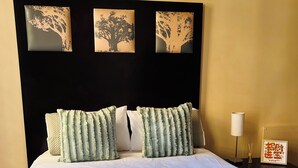 Une chambre d’hôtel comprenant un lit, des oreillers, une tête de lit décorée, une table de chevet avec une lampe et un cadre photo fixé au mur.