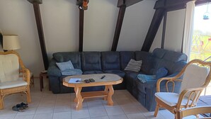 A living room with a dark leather sofa, a wooden coffee table, wicker chairs, and a lamp. - Gemutliche Unterkunft in Burhave (Butjadingen)