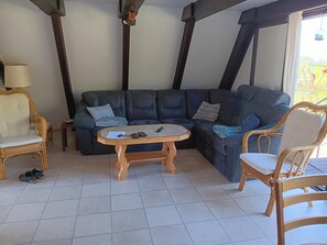 A living room with a dark leather sofa, a wooden coffee table, wicker chairs, and a lamp. - Gemutliche Unterkunft in Burhave (Butjadingen)