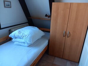 Una cama individual con ropa blanca, un armario de madera con dos puertas y un estante pequeño encima de la cama.