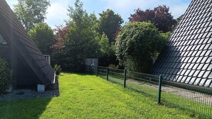 A grassy area with a fence, trees, and a building with a sloped roof. - Gemutliche Unterkunft in Burhave (Butjadingen)