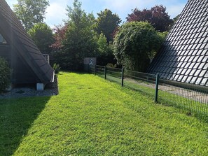 A grassy area with a fence, trees, and a building with a sloped roof. - Gemutliche Unterkunft in Burhave (Butjadingen)
