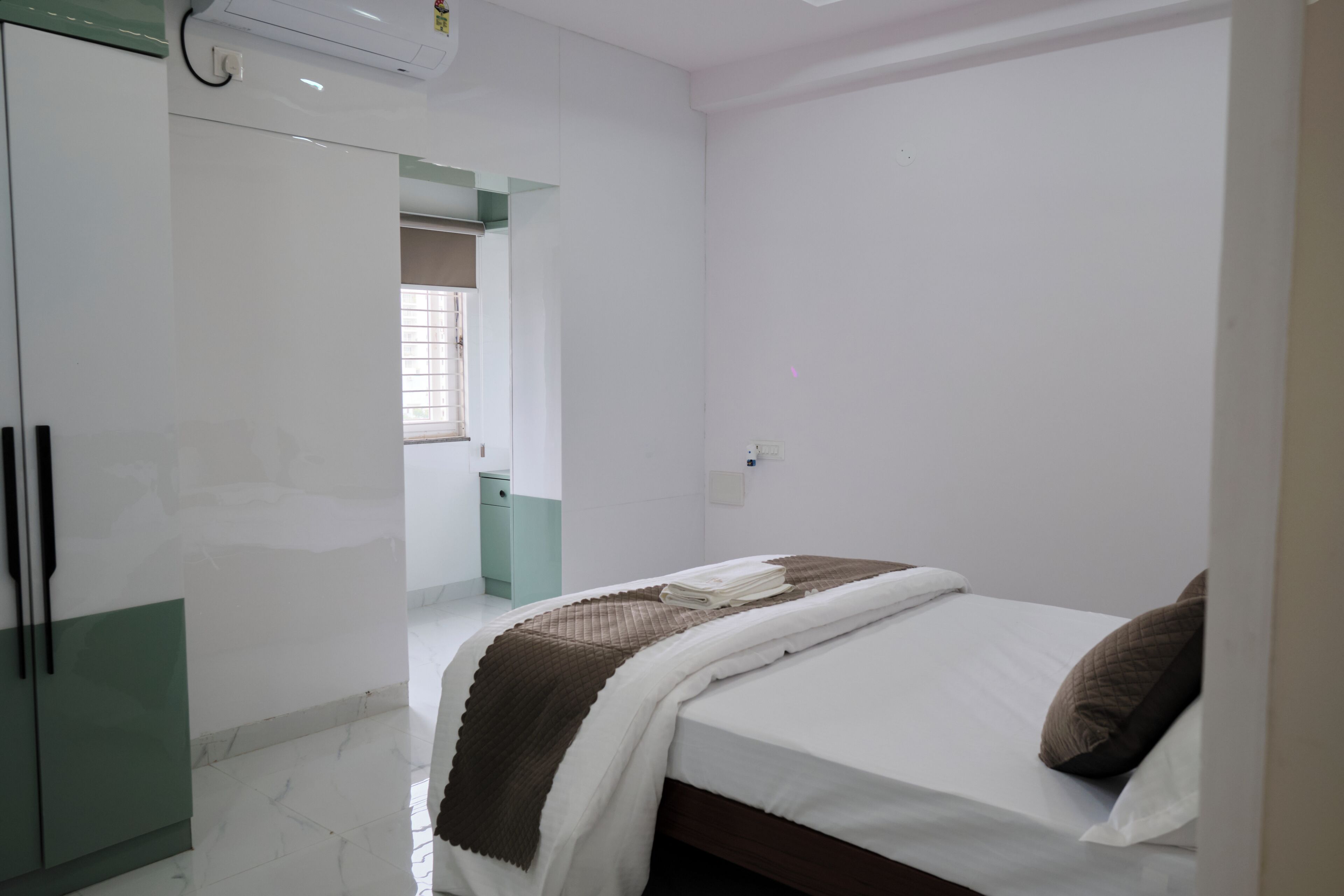 Ein Schlafzimmer mit Bett, Kleiderschrank und einem durchgehenden Türrahmen sichtbarem Badezimmer.