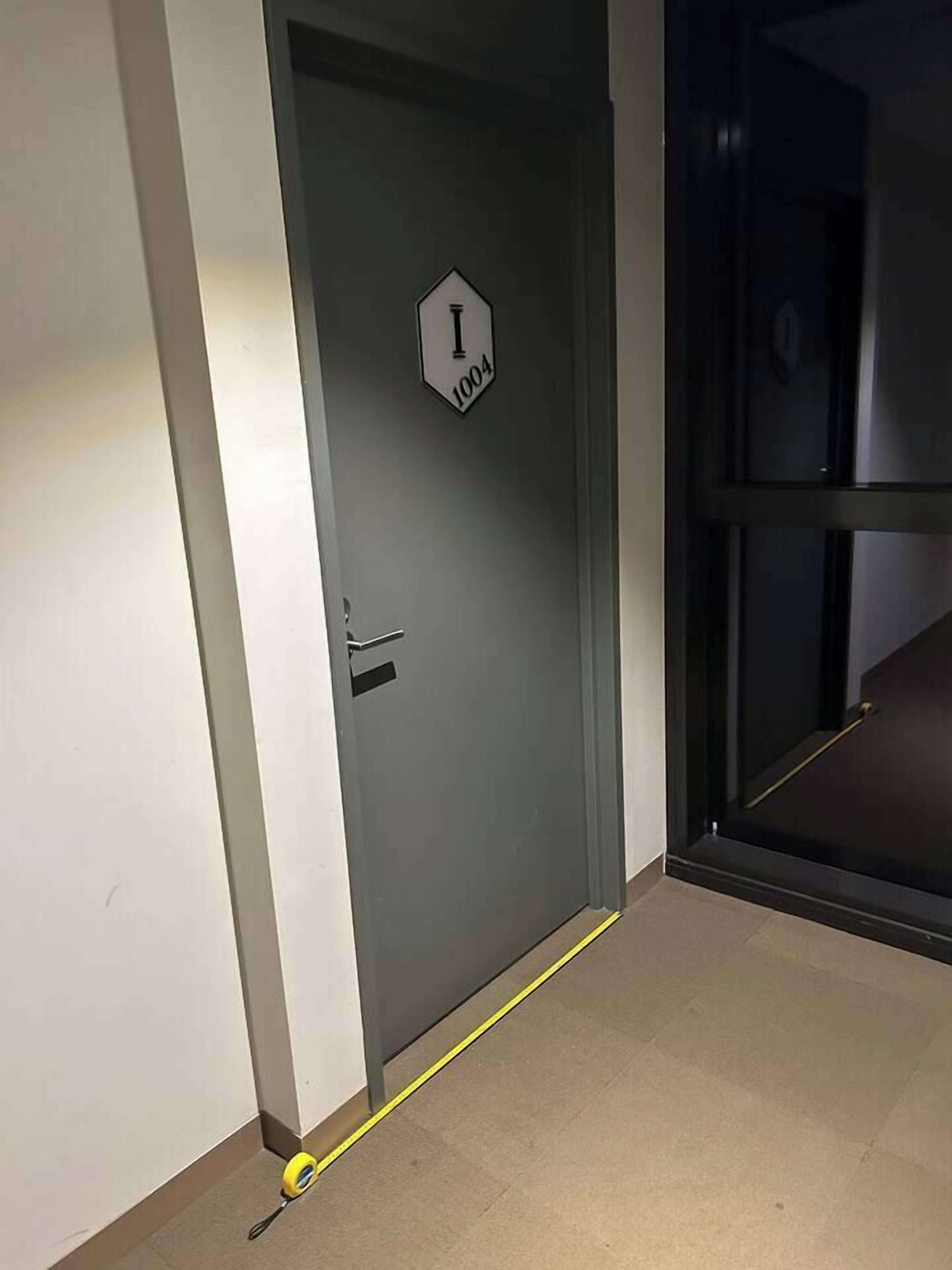 A door with a sign indicating room number 1004, a door handle, and a yellow measuring tape on the floor.