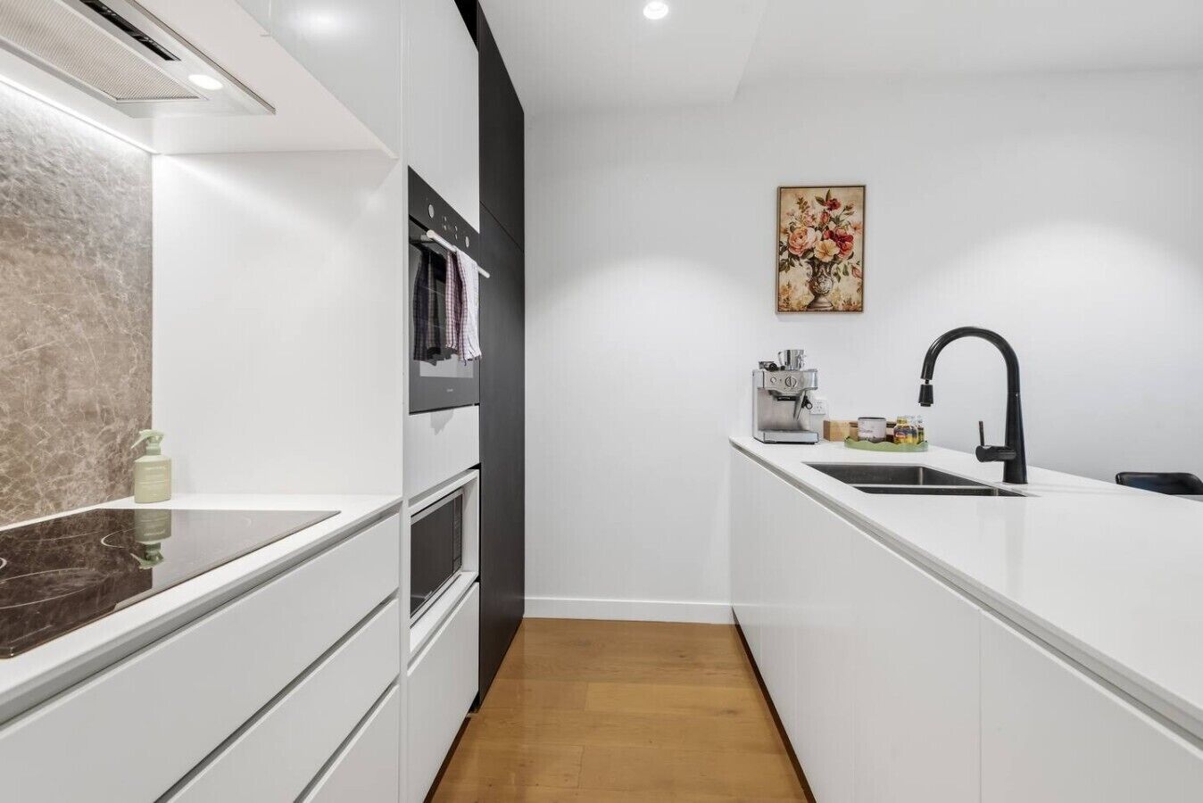 A modern kitchen with white cabinetry, a black faucet, and a wooden floor.