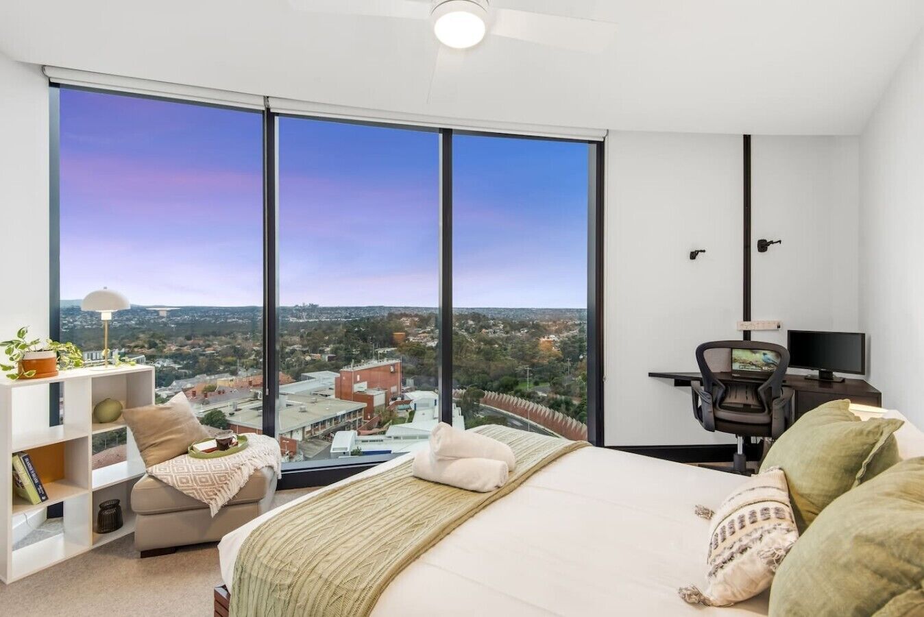 A bedroom with a large window, a bed, a desk, and a chair.