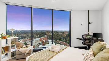 A bedroom with a large window, a bed, a desk, and a chair.