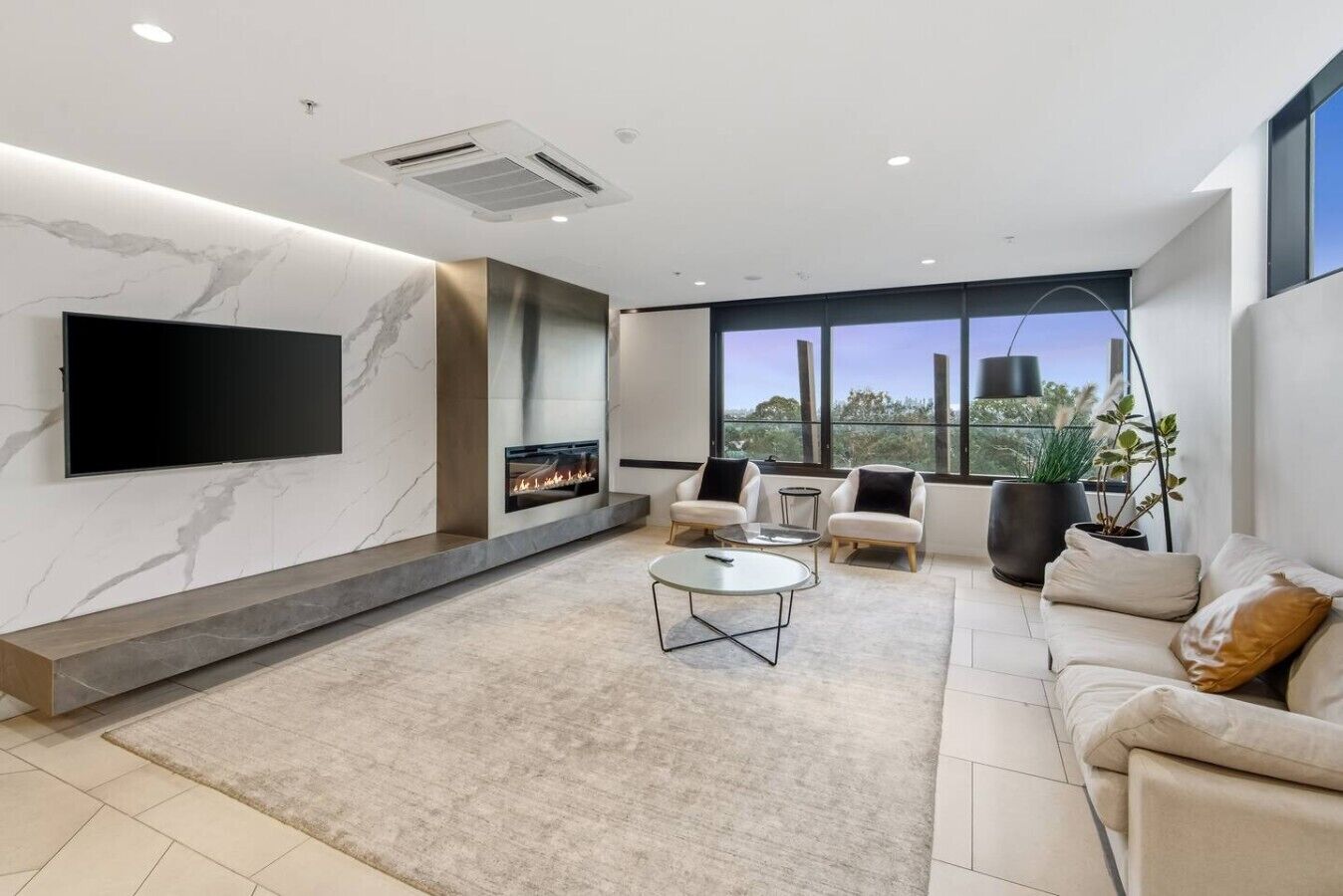 A modern living room with a fireplace, comfortable seating, a flat-screen TV, and large windows offering a view.