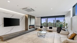 A modern living room with a fireplace, comfortable seating, a flat-screen TV, and large windows offering a view. - Austin Hospital | City views | Gym & Pool | 2B1B (Ivanhoe)