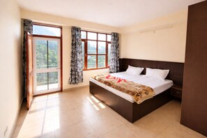 Ein Schlafzimmer mit Bett, Vorhängen, einem Fenster und Blick ins Grüne.