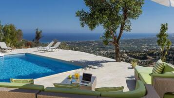 A poolside area with a view of the sea, lounge chairs, and a table with a laptop and drinks.