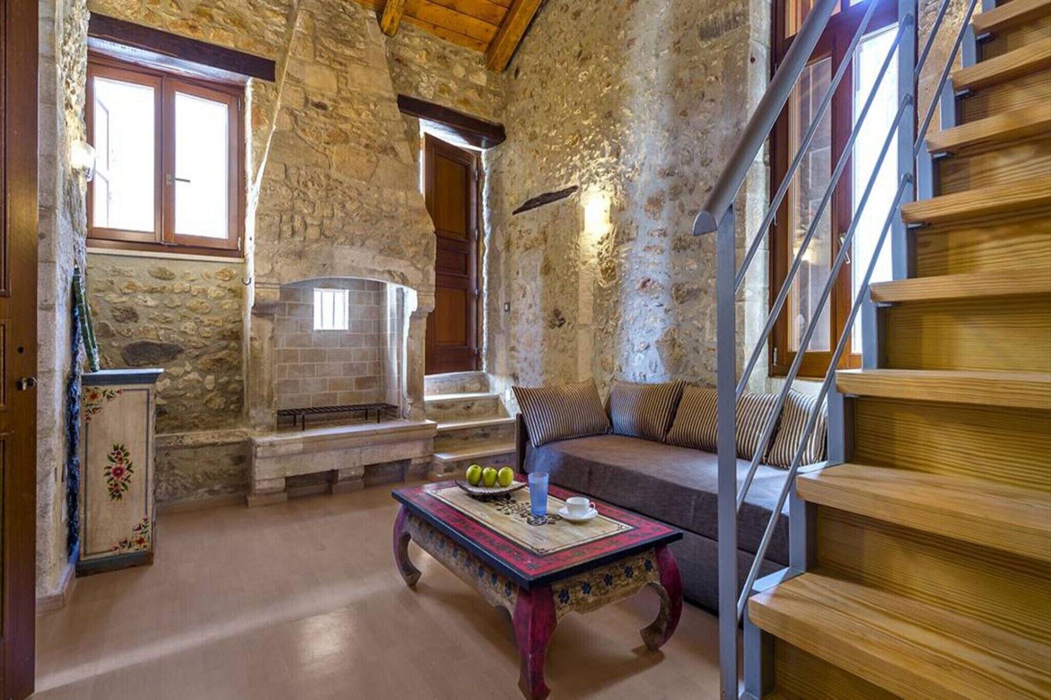 A rustic interior with a stone fireplace, wooden staircase, and a sofa with striped cushions.