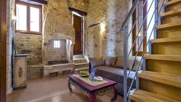 A rustic interior with a stone fireplace, wooden staircase, and a sofa with striped cushions.