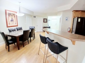 A dining area with a wooden table and chairs, a kitchen area with a countertop, and a hallway with doors. - Sunset Waterfront Resort, Executive Townhouse 113. Luxury Lakeside, 3 Bed/2 Bath (Kelowna)