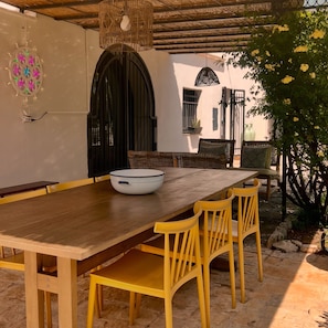 An outdoor dining area with a wooden table and yellow chairs, a woven hanging light fixture, and a black gate. - Le Lamie di Ostuni - a traditional country house with a pool (Puglia)