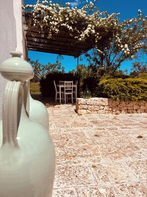 Eine Steinterrasse mit Tisch und Stühlen unter einer Pergola mit weißen Blüten.