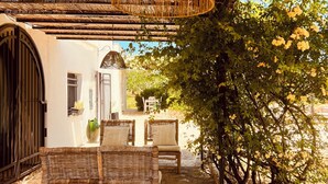 An outdoor dining area with a wooden table and chairs, a hanging light fixture, and a view of a garden with trees and a building in the background. - Le Lamie di Ostuni - a traditional country house with a pool (Puglia)