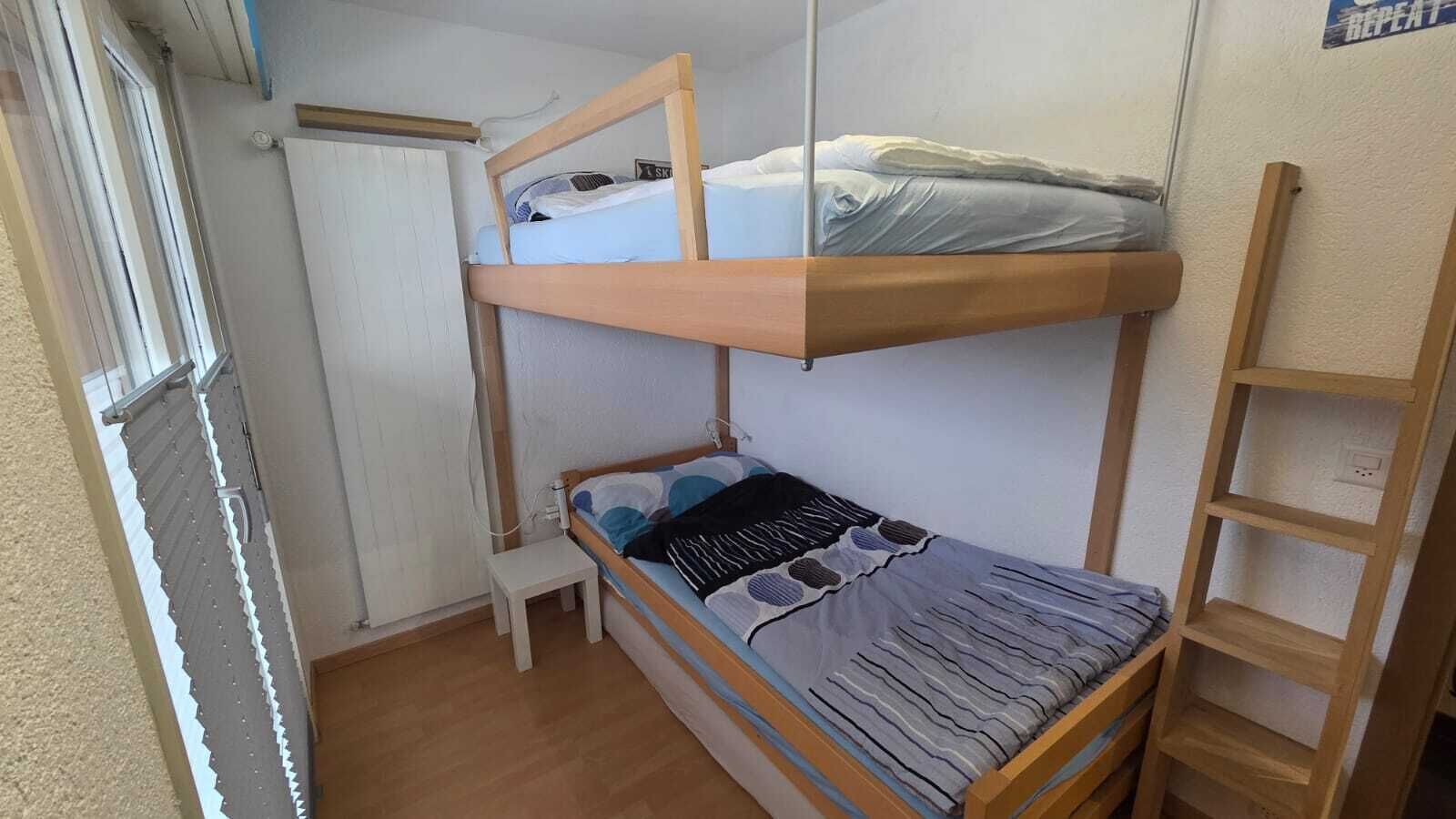 Un lit superposé avec un lit inférieur, une petite table de chevet et une échelle en bois.