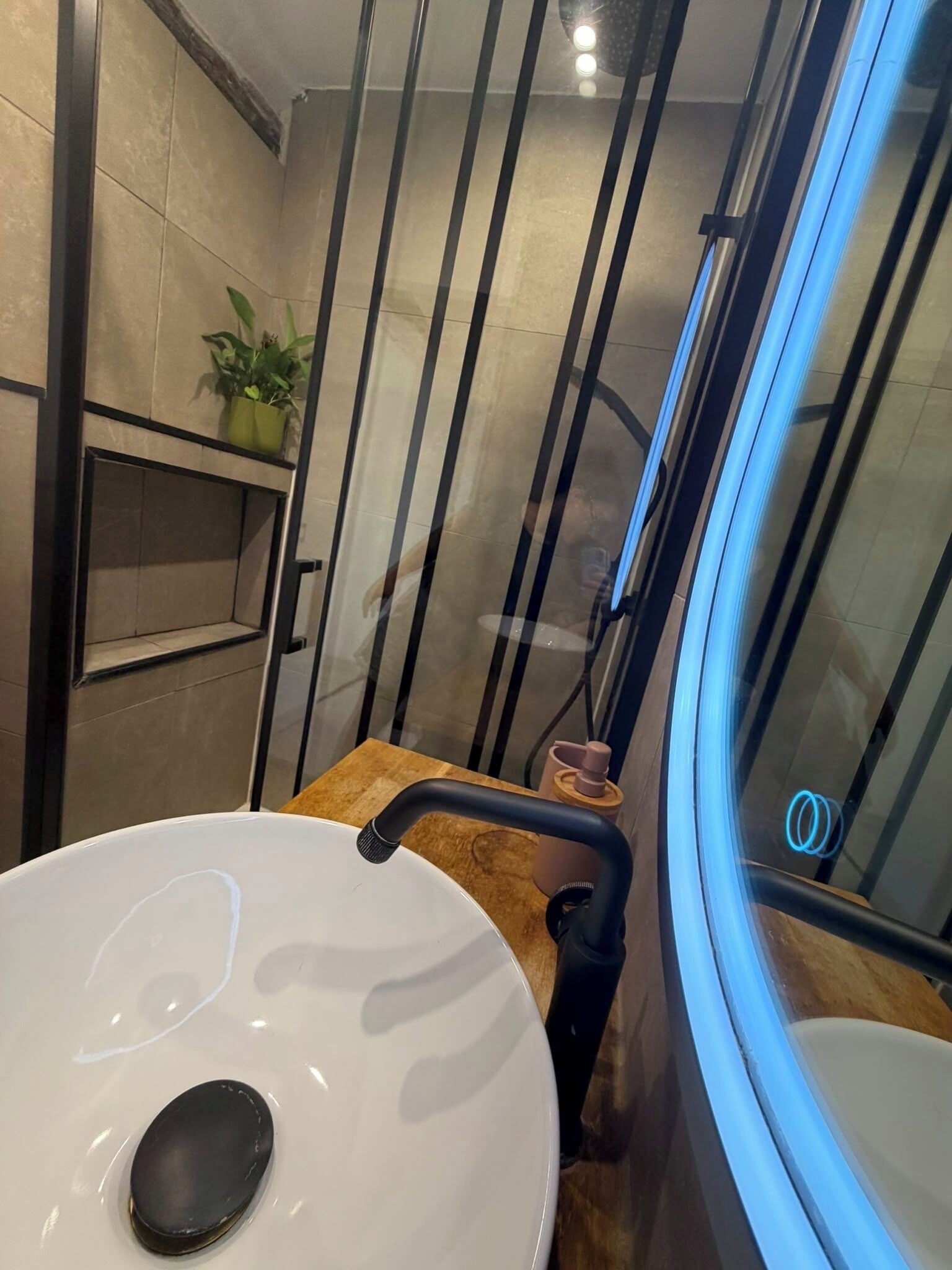 Un baño con lavamanos blanco, encimera de madera, cabina de ducha de cristal y una planta en maceta.