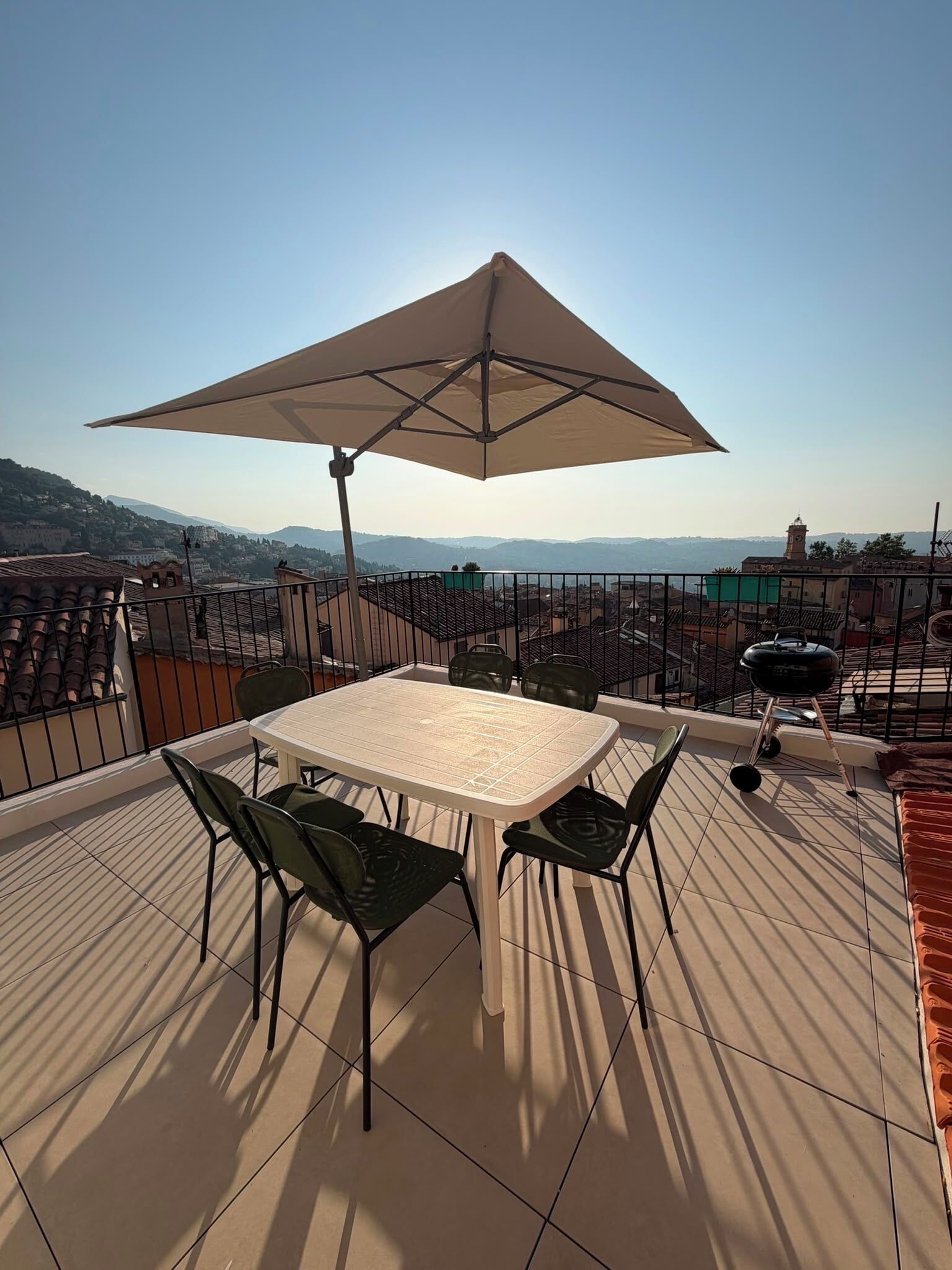 Eine Terrasse mit Tisch und Stühlen, einem großen Sonnenschirm und Blick auf eine Stadtansicht.