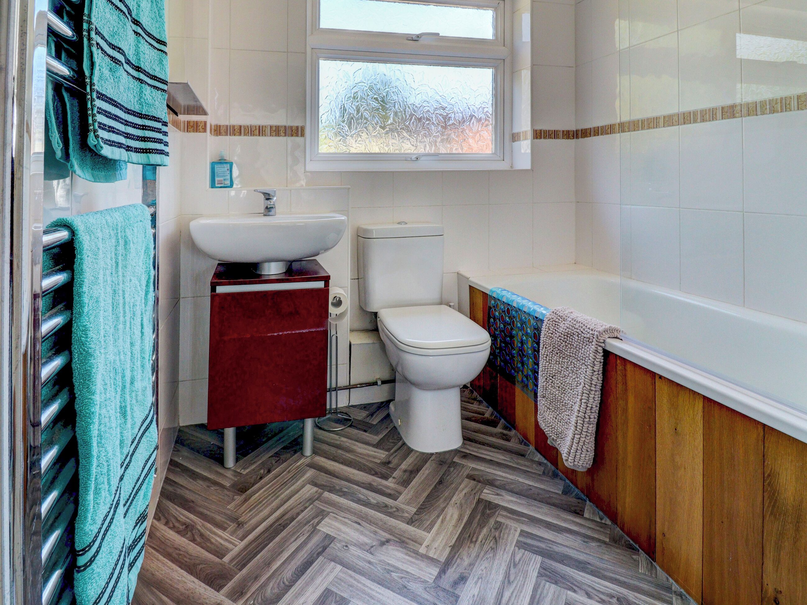 A bathroom with a herringbone floor, a white toilet, a sink, and a bathtub.
