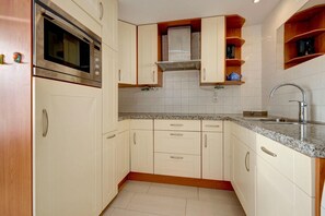 A compact kitchen with a built-in oven, a sink, and wooden cabinets. - Holiday Home in South Holland (Noordwijkerhout)