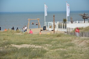 Un endroit situé au bord de la plage, équipé d’une balançoire, d’un espace délimité par une clôture et de drapeaux.