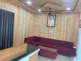 Una habitación con paredes de paneles de madera, un sofá rojo, un escritorio de madera y un ventilador de techo.