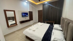 Habitación de hotel con cama, televisión montada en la pared, ventilador de techo y ventana con cortinas.
