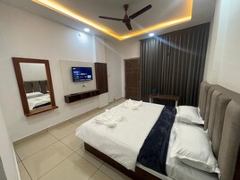 Habitación de hotel con cama, televisión montada en la pared, ventilador de techo y ventana con cortinas.