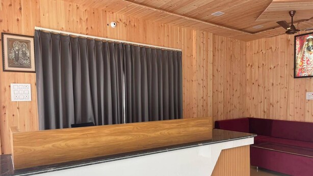 Un mostrador de recepción con detalles de madera, una cortina oscura y un sofá rojo en una sala con paneles de madera.
