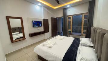 A hotel room with a bed, a television, a ceiling fan, and a window with curtains.