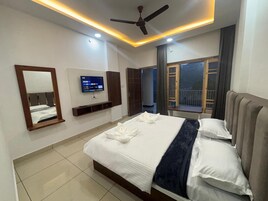 Habitación de hotel con cama, televisor, ventilador de techo y ventana con cortinas.
