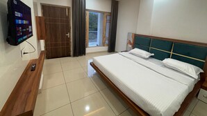 Habitación de hotel con cama, televisión montada en la pared, ventilador de techo y ventana con cortinas.