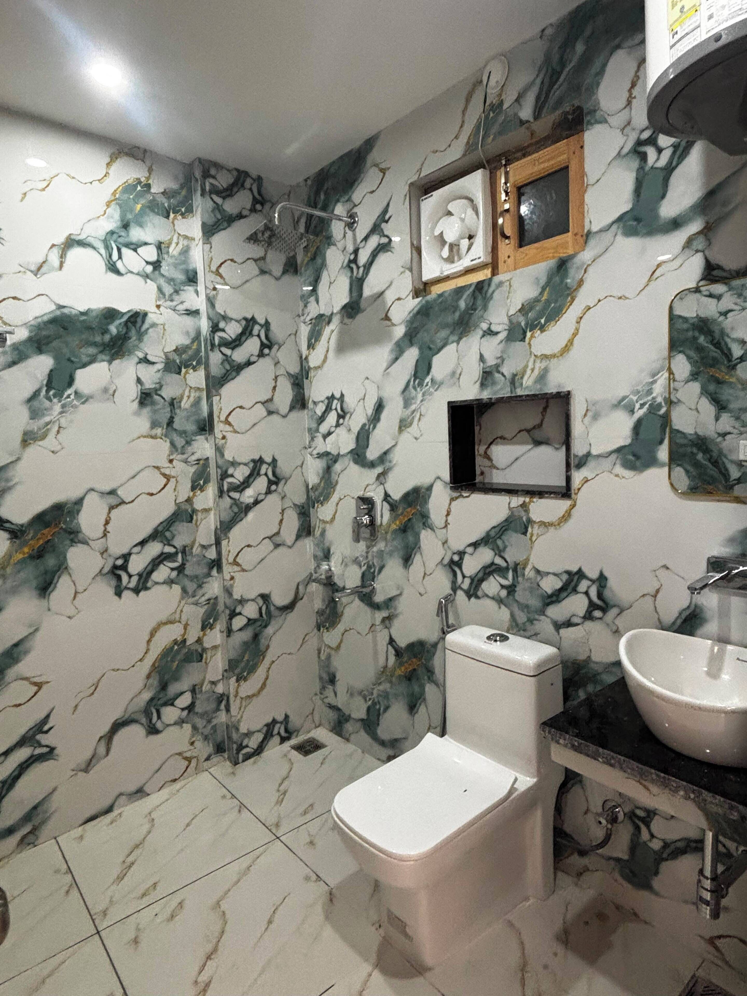 A bathroom with a marble wall design, a toilet, a sink, and a shower.