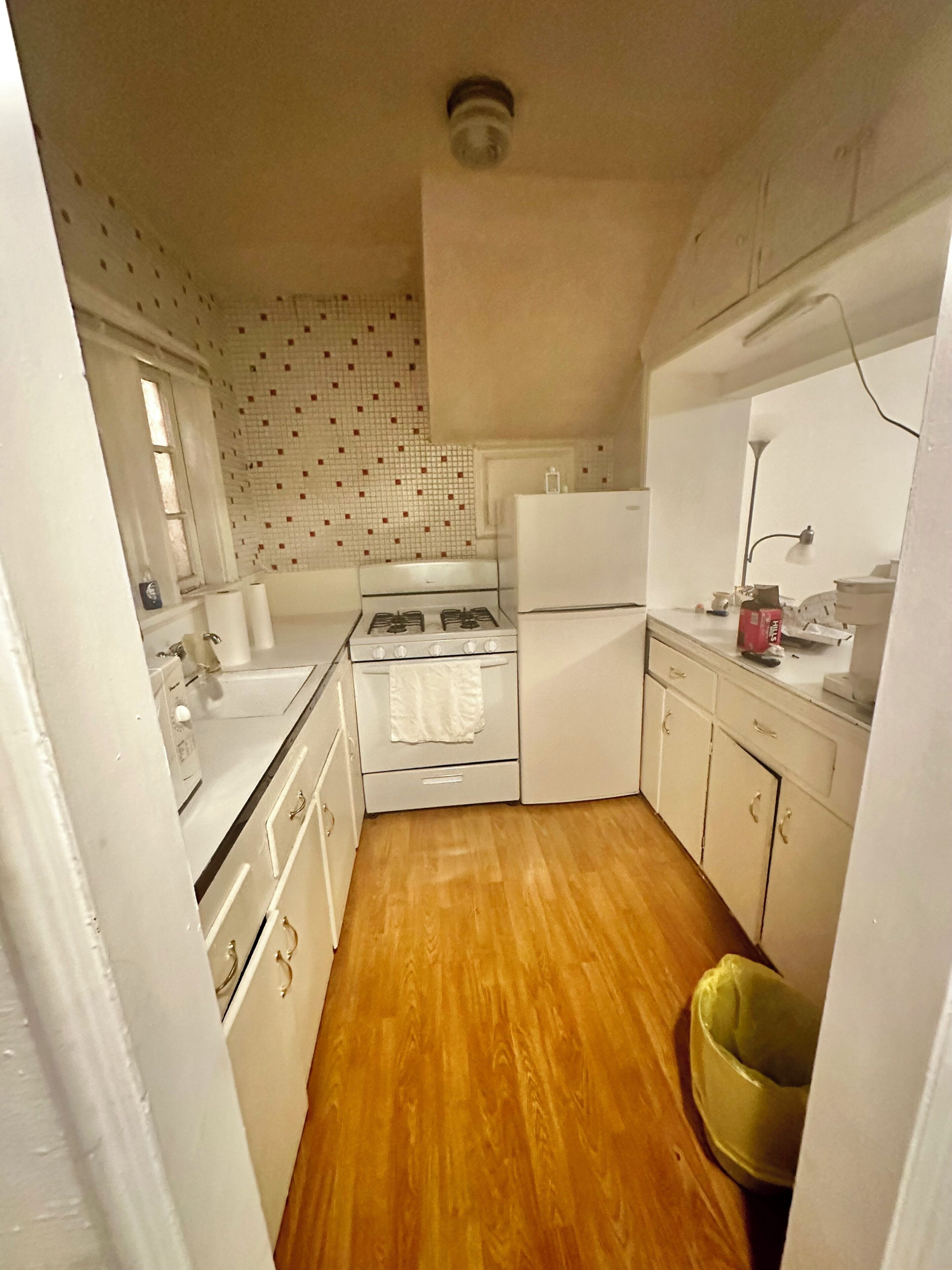 Cocina compacta con estufa, horno y refrigerador, piso de madera y salpicadero de azulejos.