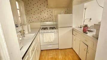 Cocina compacta con estufa, horno y refrigerador, piso de madera y salpicadero de azulejos.