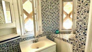 Un baño con lavamanos blanco, dos espejos y una ventana.