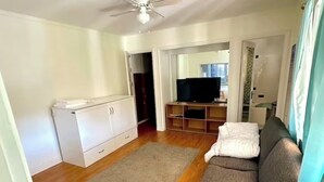 Una sala de estar con sofá, televisor, ventilador de techo y piso de madera.