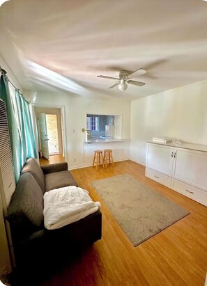 A living room with a sofa, a ceiling fan, a kitchen area with stools, and a window. - Charming retro studio in Hollywood Hills with views - close to top attractions (Los Angeles)