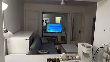 A compact living space with a kitchenette, a sofa, a television, and a coffee maker.