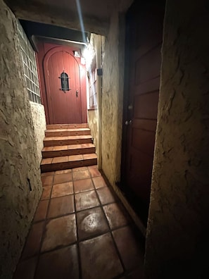 A narrow stairway leading to a red door with a small window, flanked by textured walls and a tiled floor. - Charming retro studio in Hollywood Hills with views - close to top attractions (Los Angeles)